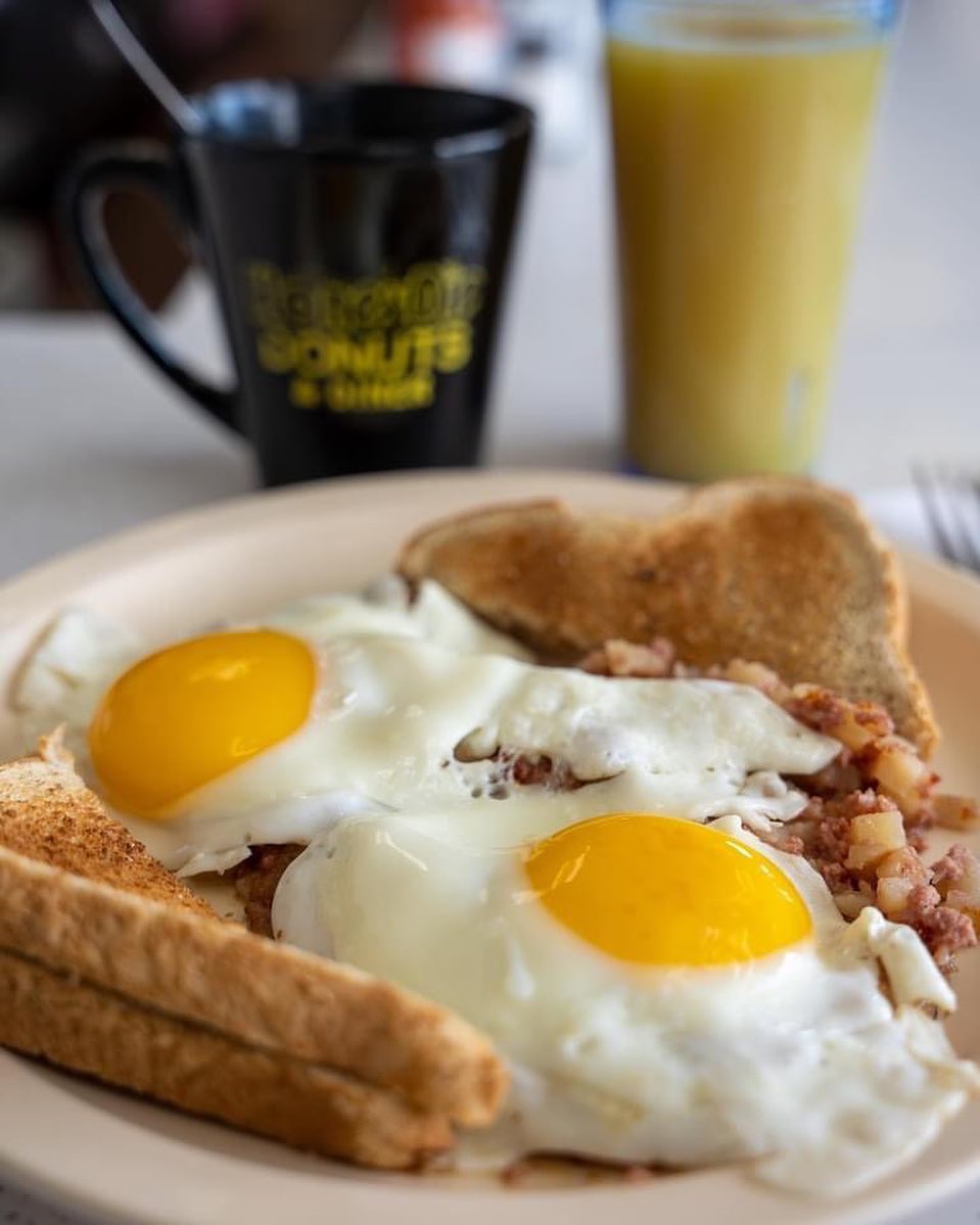 Two sunny-side-up eggs with corned beef hash and toast, a HoneyDip mug behind